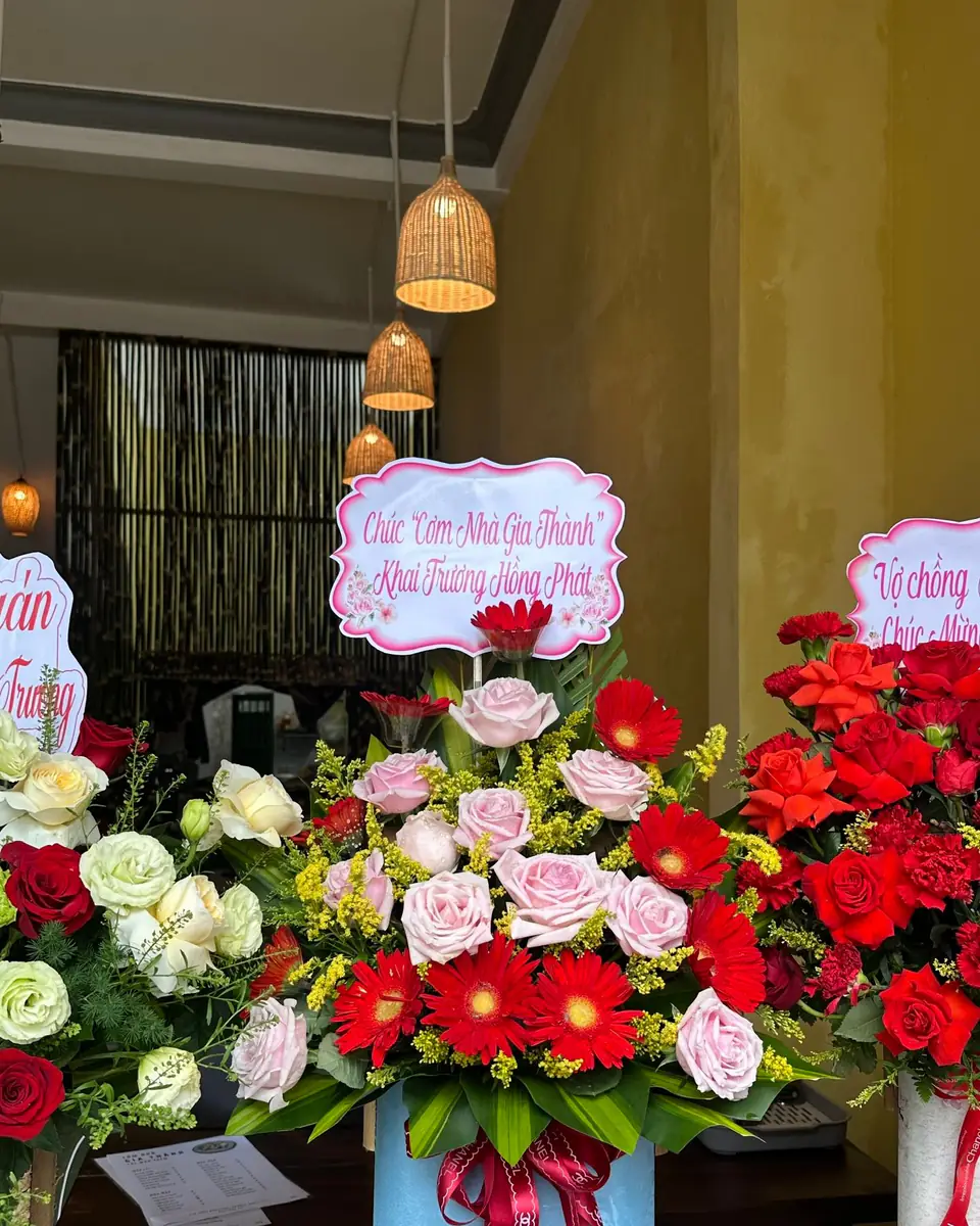 Bình hoa hồng phấn và đồng tiền đỏ cắm trong hộp xanh, thắt nơ đỏ
