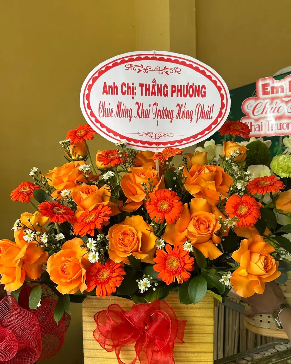 Giỏ hoa để bàn tông cam rực rỡ, hoa hồng cam và đồng tiền, nơ đỏ