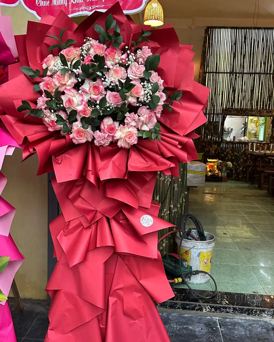 Kệ hoa khai trương tông hồng đỏ, bó hồng phấn trên nền giấy gói đỏ xếp nếp