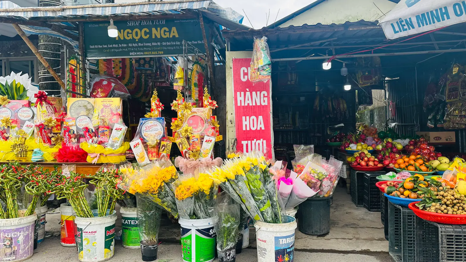 Mặt tiền sạp hoa Ngọc Nga với hoa cúc vàng, hoa bó và đồ lễ bày phía trước